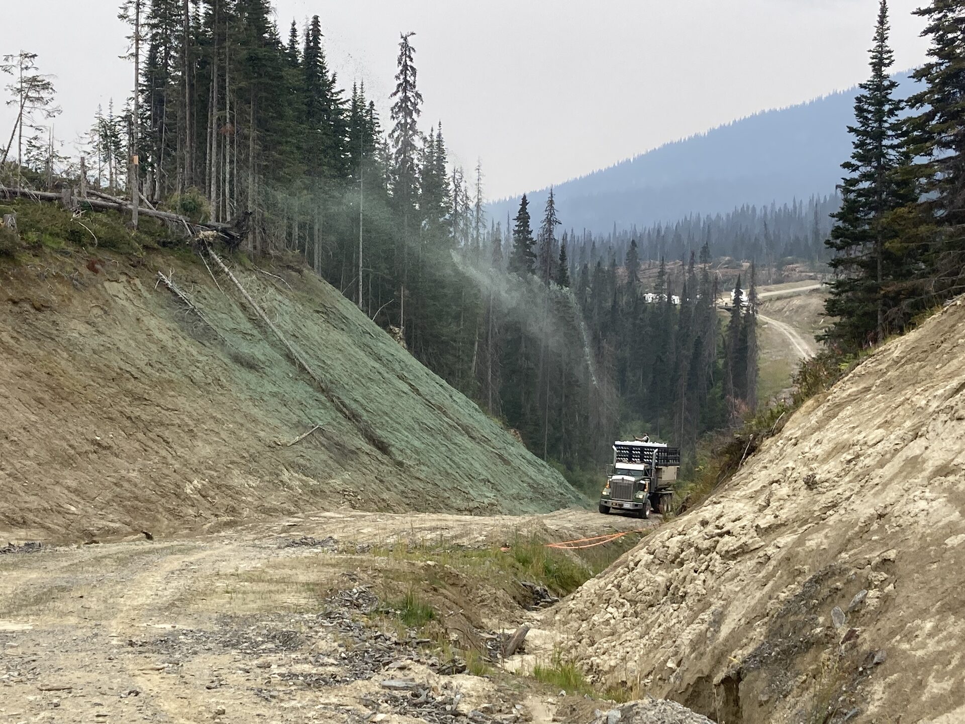 Hydroseeding crew spraying a steep cut slope along a mountain road corridor, BC