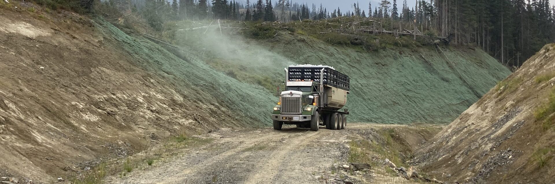Hydroseeder truck on a resource road flanked by freshly seeded green slopes, BC